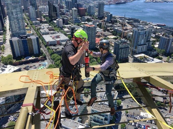 Two riggers harnessed on an exposed beam high above Seattle, preparing the Stratos bungee capture