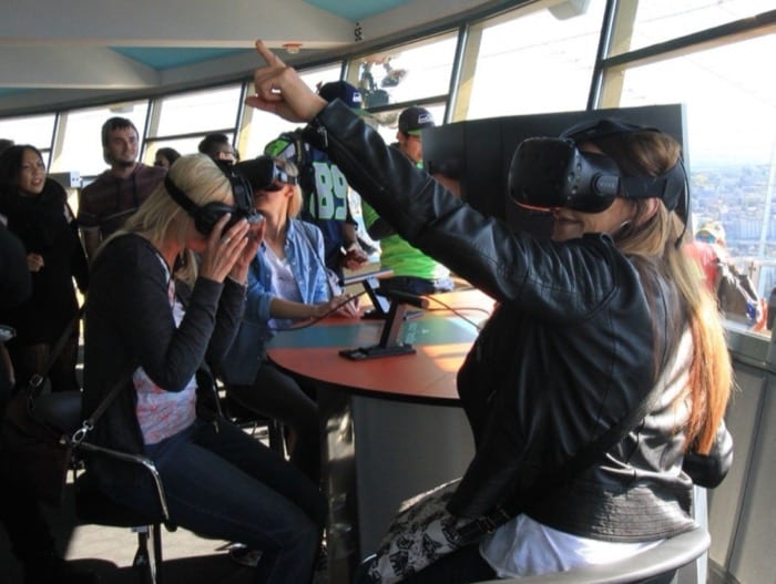 Guests wearing Oculus VR headsets at a table inside the Space Needle, with the Seattle skyline visible through the windows